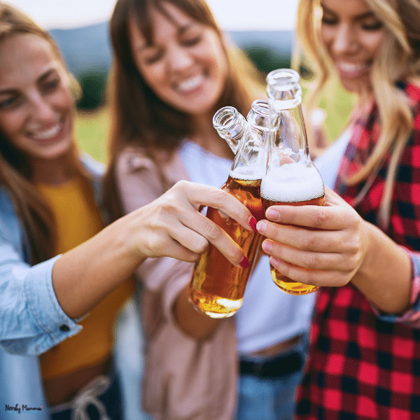 Three young women clink bottles of amber-colored drinks outdoors, illustrating social situations that may concern parents who suspect their teen is drinking.