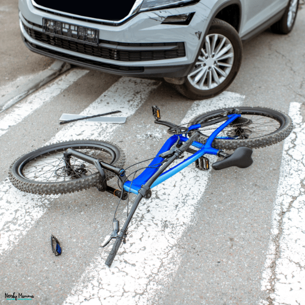 A blue bicycle and scattered debris lie near the damaged front bumper of a silver SUV after a cyclist accident.