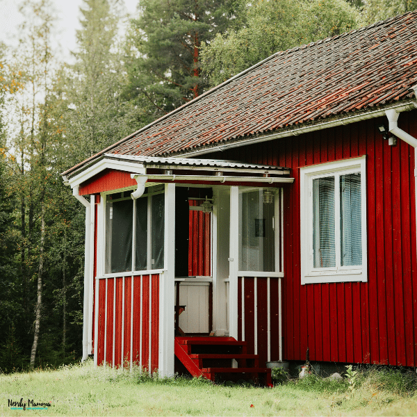 Small home with red wooden siding, white trim, a weathered tile roof, and a screened entry porch surrounded by trees.