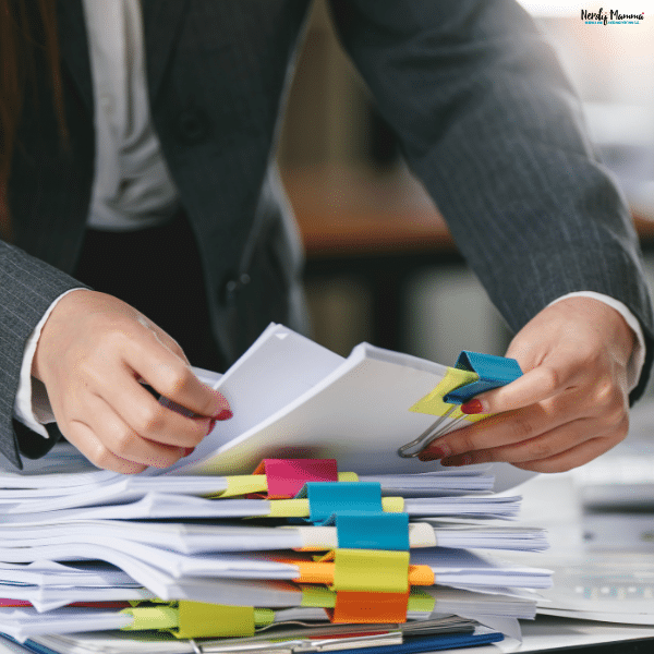 A person in a gray suit organizes business paperwork into stacks secured with colorful binder clips.