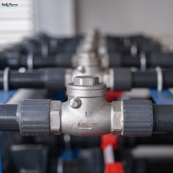 A metal check valve connects gray plastic pipes, showing a different material option from PVC check valves.