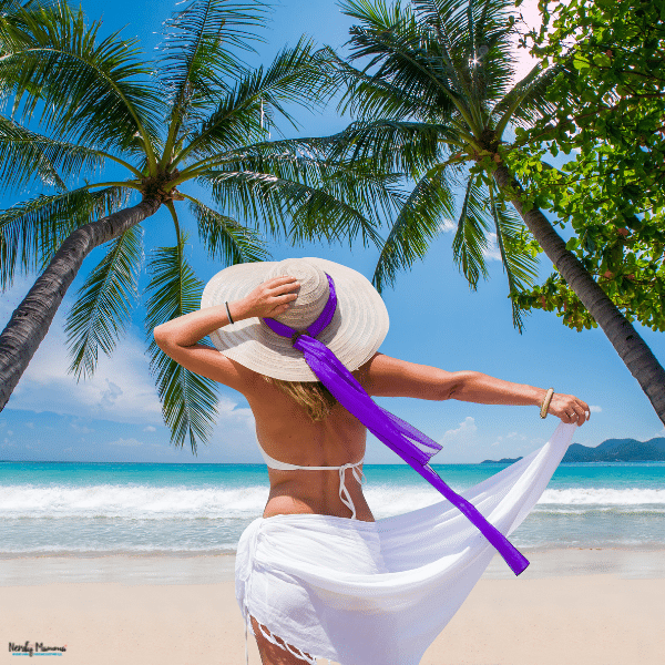 Woman stands beneath palm trees beside turquoise water, enjoying a tropical beach setting for her perfect holiday.